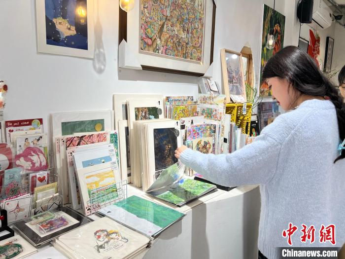 圖為藝術(shù)品商店內(nèi)，顧客挑選插畫作品?！＄婌?攝