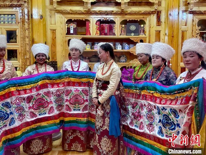 圖為女性展示村民自發繡制的“百米五彩哈達”。　李玉峰 攝